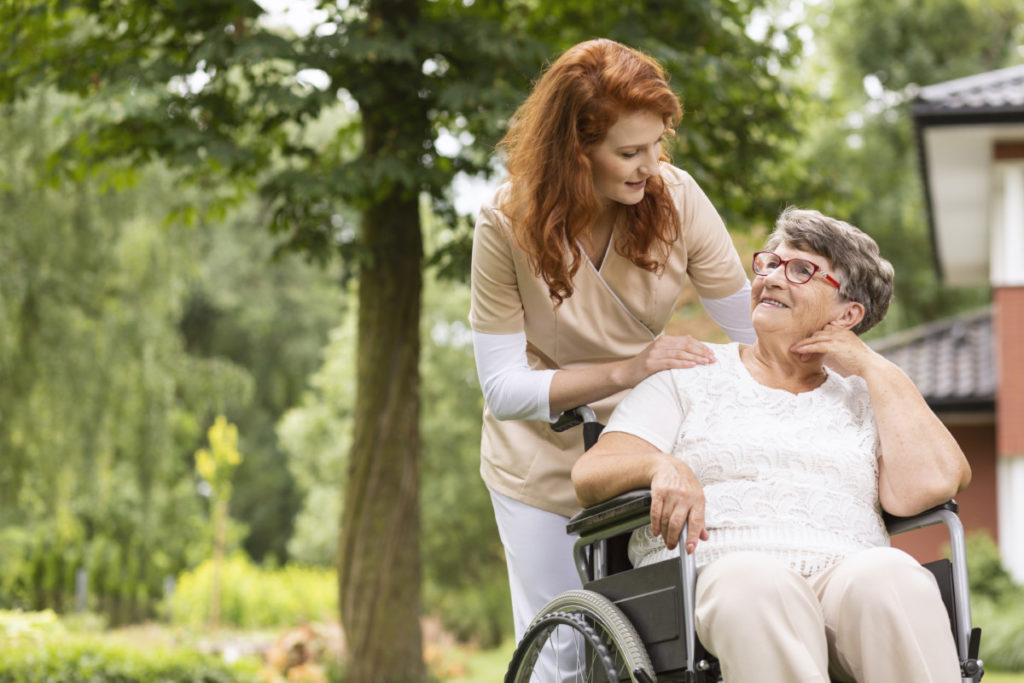 Une aide soignante qui pousse une personne en fauteuil roulant